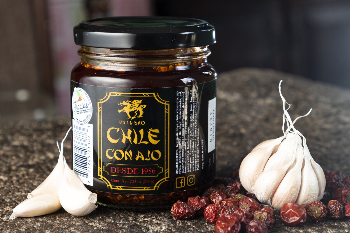 Frasco de Chile con Ajo Fu Lu Sho rodeado de chiles secos y cabezas de ajo